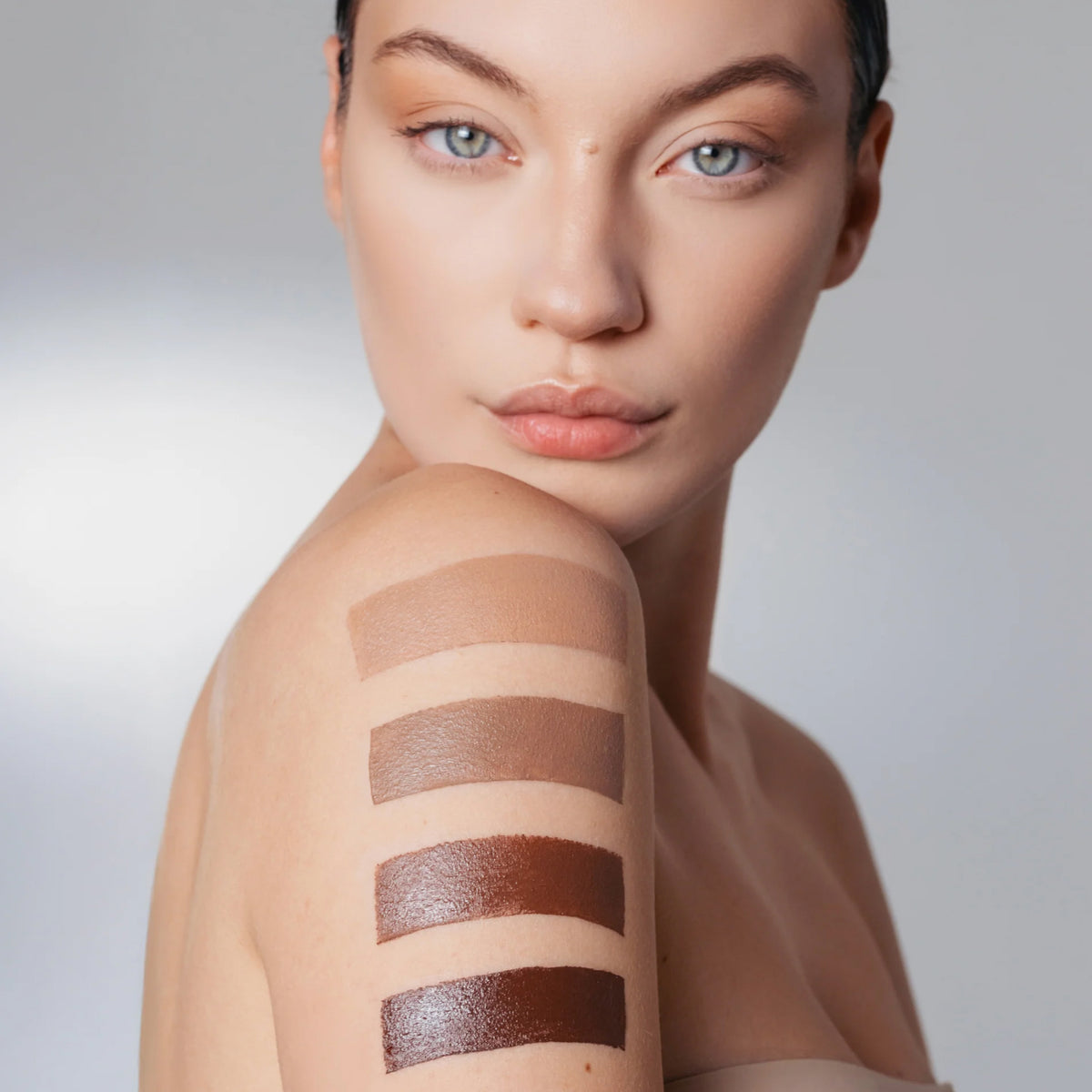 Frau mit makellosem hellen Teint, auf deren Oberarm vier cremige Swatches des The Mood Contrast in verschiedenen Brauntönen aufgetragen sind.
