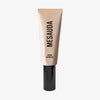 Eine beigefarbene Tube mit der Aufschrift "Dew Shield" von Mesauda Beauty mit einer schwarzen Kappe, die aufrecht auf einem weißen Hintergrund steht.
