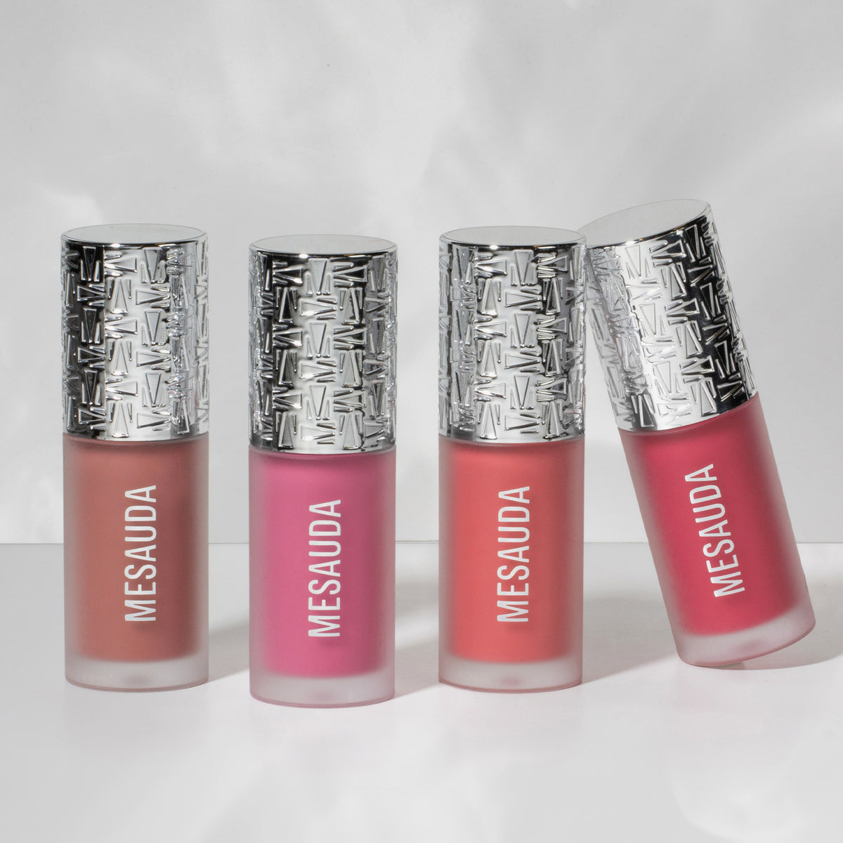 Vier „Flush of Blush“-Flaschen von Mesauda Milano mit silbergemusterter Kappen, aufgereiht vor einem hellen Hintergrund.