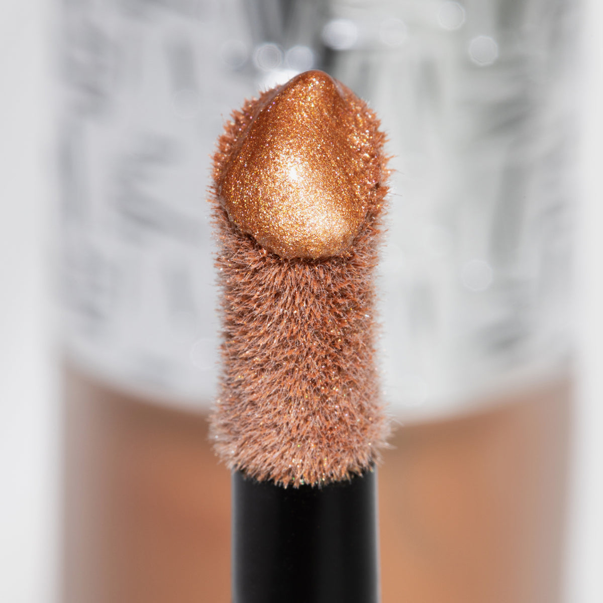 Nahaufnahme des Highlighter-Applikators; darauf ein Tropfen Flush of Light Sunset Bronze mit strukturierter silber Kappe im Hintergrund.