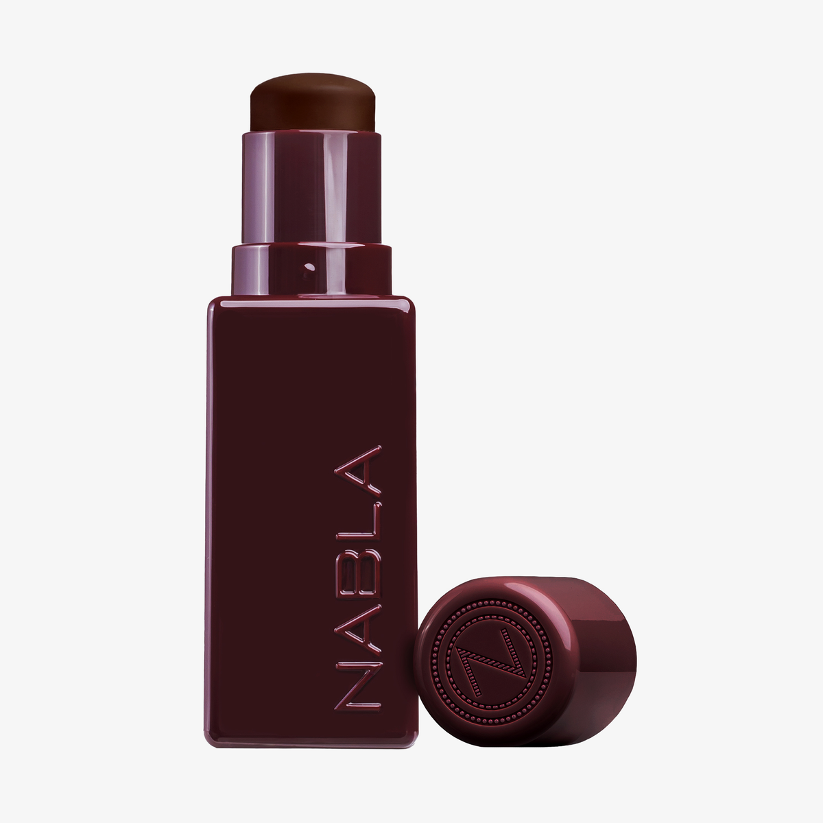 Der NABLA Cosmetics Art Of Skin Foundation Stick ist in einer quadratischen Tube mit NABLA-Schriftzug abgebildet, die Kappe befindet sich in der Nähe.