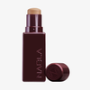Eine burgunderfarbene Tube NABLA Cosmetics Art Of Skin Foundation Stick mit abgenommener Kappe, die daneben gelegt wird.