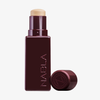 Eine burgunderfarbene Tube NABLA Cosmetics Art Of Skin Foundation Stick mit abgenommener Kappe, die das beigefarbene Produkt im Inneren enthüllt.