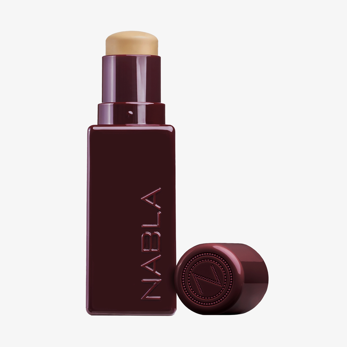 Eine burgunderfarbene Tube des NABLA Cosmetics Art Of Skin Foundation Stick mit abgenommener Kappe, die die beigefarbene Foundation im Inneren zeigt.