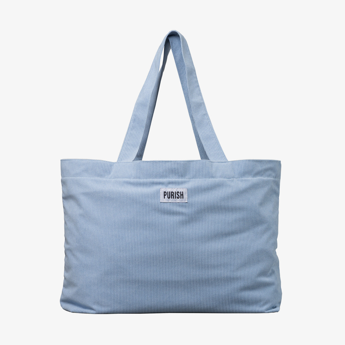 Die PURISH Beach Bag ist eine hellblaue Stofftasche mit „PURISH“ Patch auf der Vorderseite und zwei langen Schultergurten.