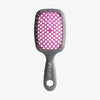 Die UNbrush Detangling Hair Brush hat einen grauen Griff mit dem UNbrush"-Schriftzug, ein pinkfarbenes Kissen und breite Borsten zum leichten Entwirren.