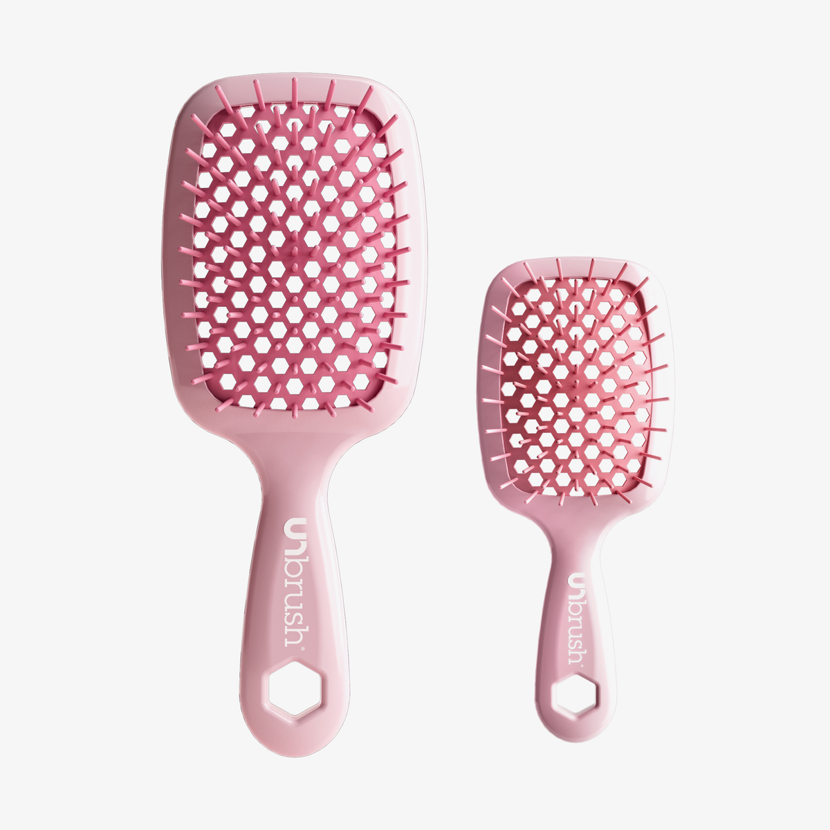Das UNbrush Pastel Duo Set besteht aus zwei rosafarbenen, belüfteten Haarbürsten in verschiedenen Größen mit sechseckigen Grifflöchern, die auf einem weißen Hintergrund abgebildet sind.