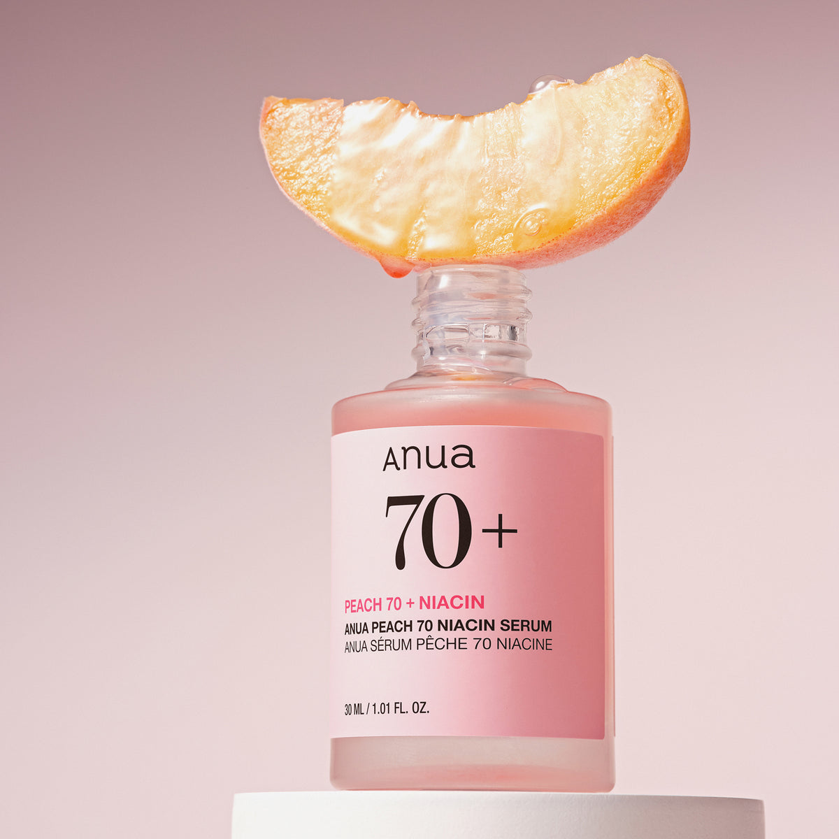 Eine Pfirsichscheibe liegt auf einer offenen Flasche Peach 70 % Niacinamide Serum vor einem zartrosa Hintergrund.