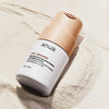 Eine Flasche Rice Enzyme Brightening Cleansing Powder liegt auf einer strukturierten, sandigen Oberfläche.