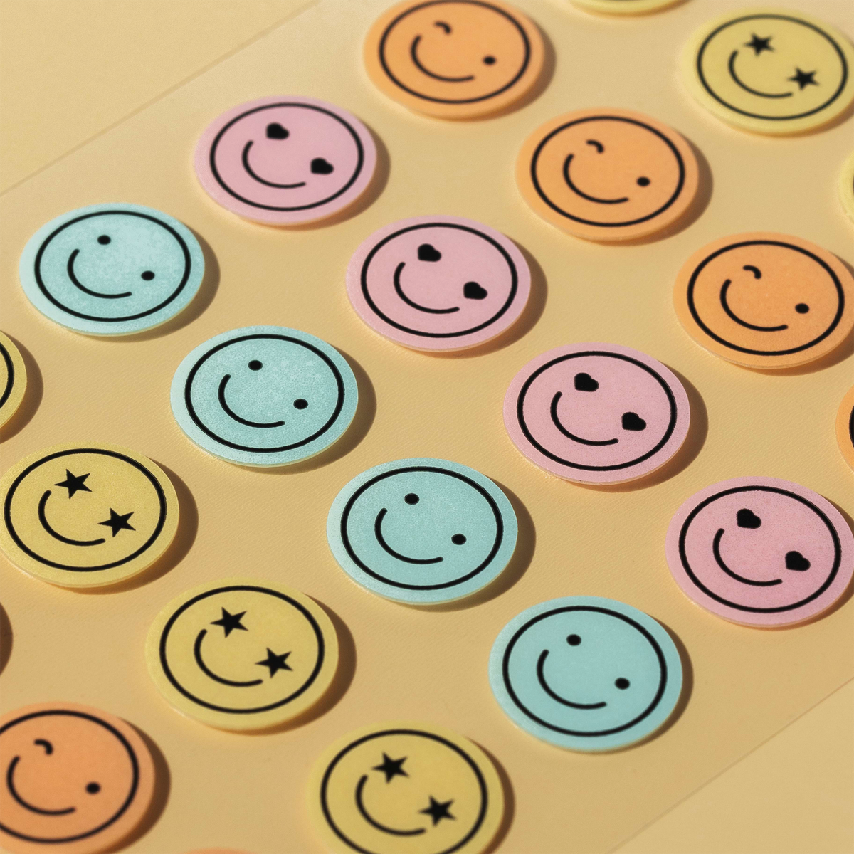Ein Bogen mit bunten, runden Mood Dots-Aufklebern, auf denen verschiedene Smileys mit Herz- oder Sternaugen abgebildet sind.