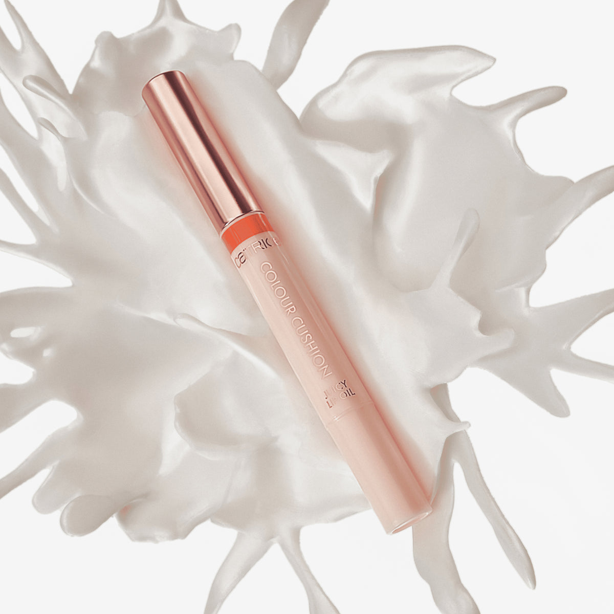 Das Colour Cushion Juicy Lip Oil mit rosafarbener Tube und roségoldener Kappe ist auf einem weiß gespritzten Flüssigkeitsuntergrund abgebildet.