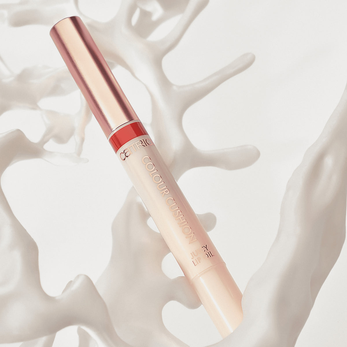 Catrice Colour Cushion Juicy Lip Oil in einem schlichten, eleganten Stift-Design mit rotem Detail, dekorativ in weißen organischen Strukturen platziert.