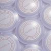 Mehrere NABLA-Puderdosen mit der Aufschrift ‚Close-Up Blotting Pressed Powder‘ in fliederfarbener Verpackung von oben fotografiert.