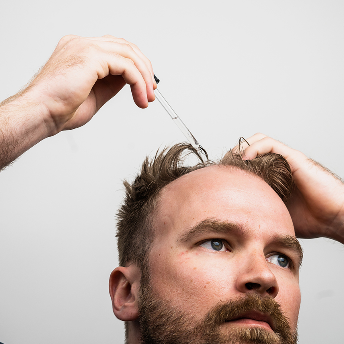 Ein Mann trägt das Bio Plixin Serum+ Men von Scandinavian Biolabs mit einer Pipette vor einem schlichten Hintergrund auf seine Kopfhaut auf.