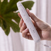 Eine Hand hält einen weißen STYLPRO Bite Pen mit Tasten, neben einem grünen Blatt im Hintergrund.