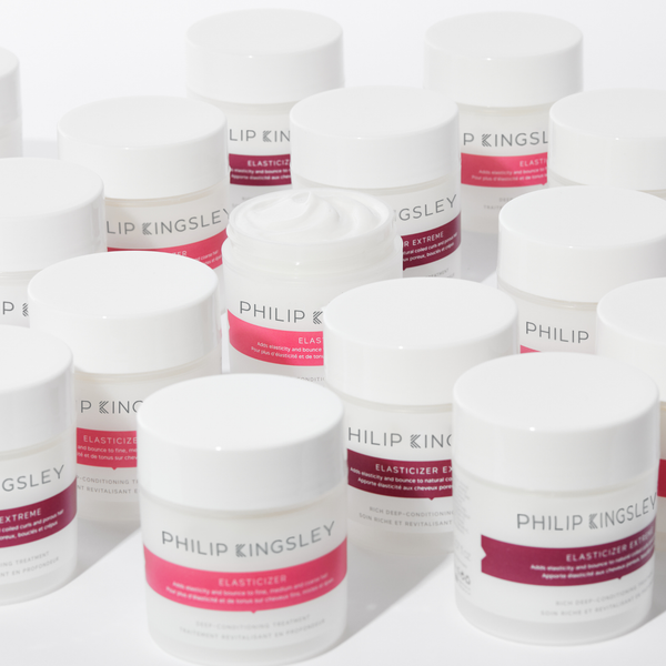 Mehrere weiße Tiegel mit der Haarpflege „Elasticizer“ von Philip Kingsley stehen nebeneinander, wobei ein Tiegel geöffnet ist und den Inhalt der Creme sichtbar macht.