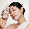 Lächelnde Frau, die vor einem hellen Hintergrund eine Flasche Rice 70 Glow Milky Toner nah an ihr Gesicht hält.