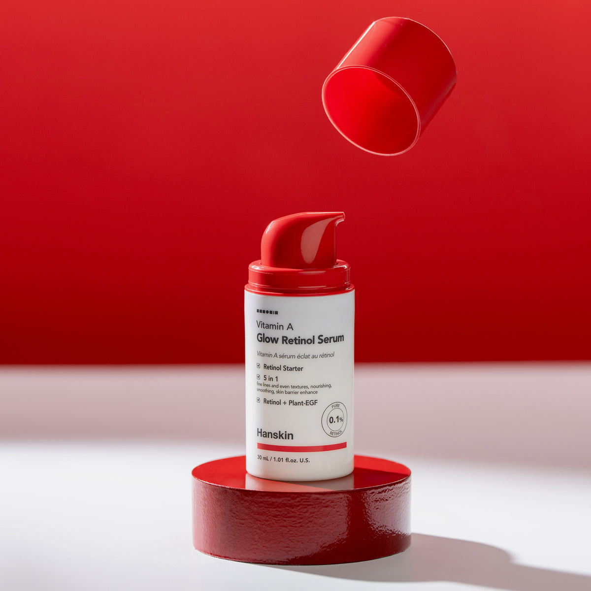 Auf einer roten Plattform wird eine Flasche Vitamin A Glow Retinol Serum mit rotem Deckel präsentiert.