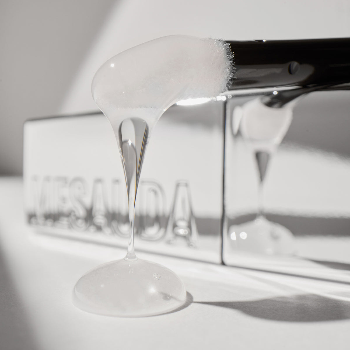 Klares Gel, das von dem Applikator tropft, mit einem reflektierenden Mesauda Beauty LIP PHENOM™ Behälter im Hintergrund.