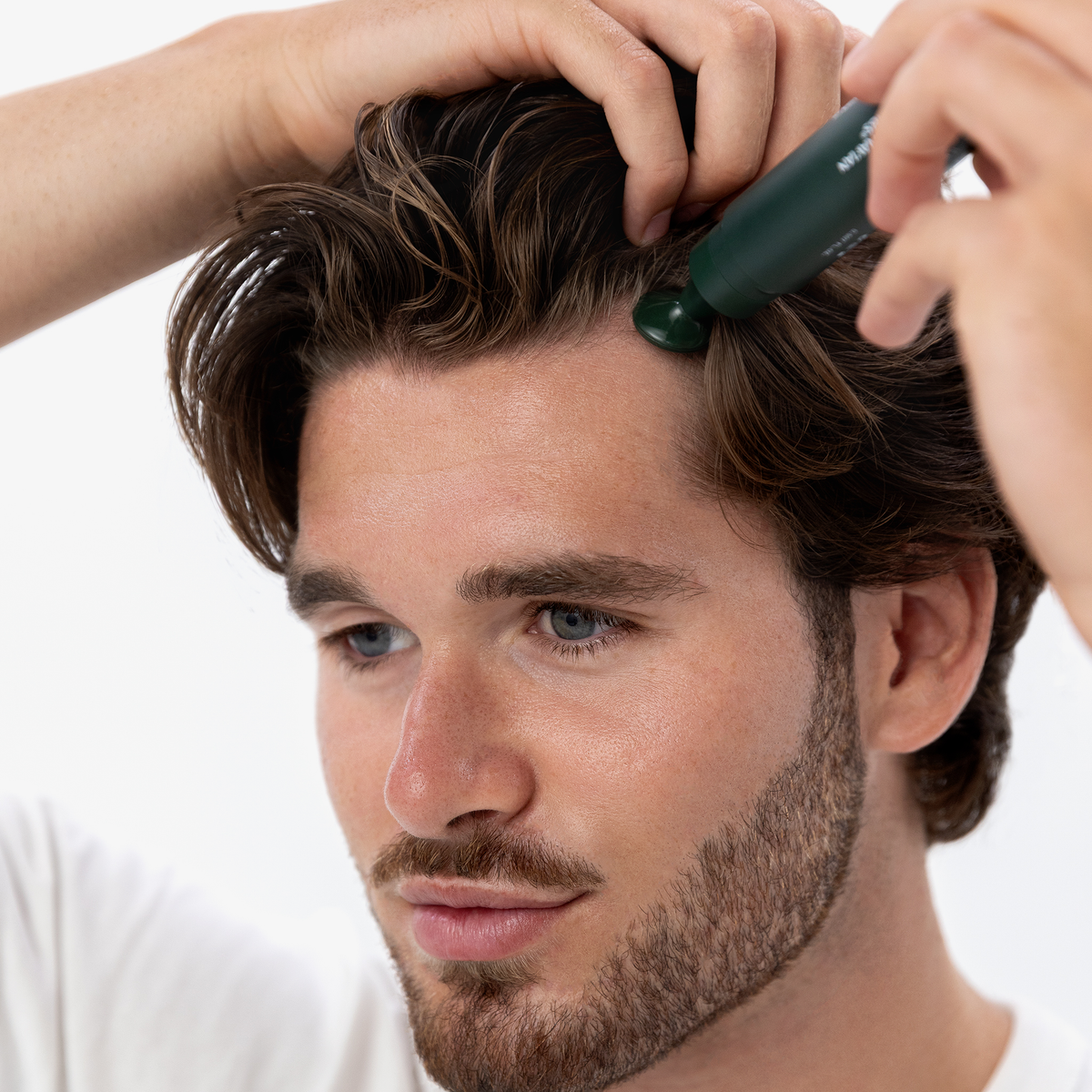 Ein Mann trägt Bio-Pilixin® Hairline Booster von Scandinavian Biolabs mit einem grünen Applikator auf seinen Haaransatz auf und hält sein Haar mit einer Hand zurück.