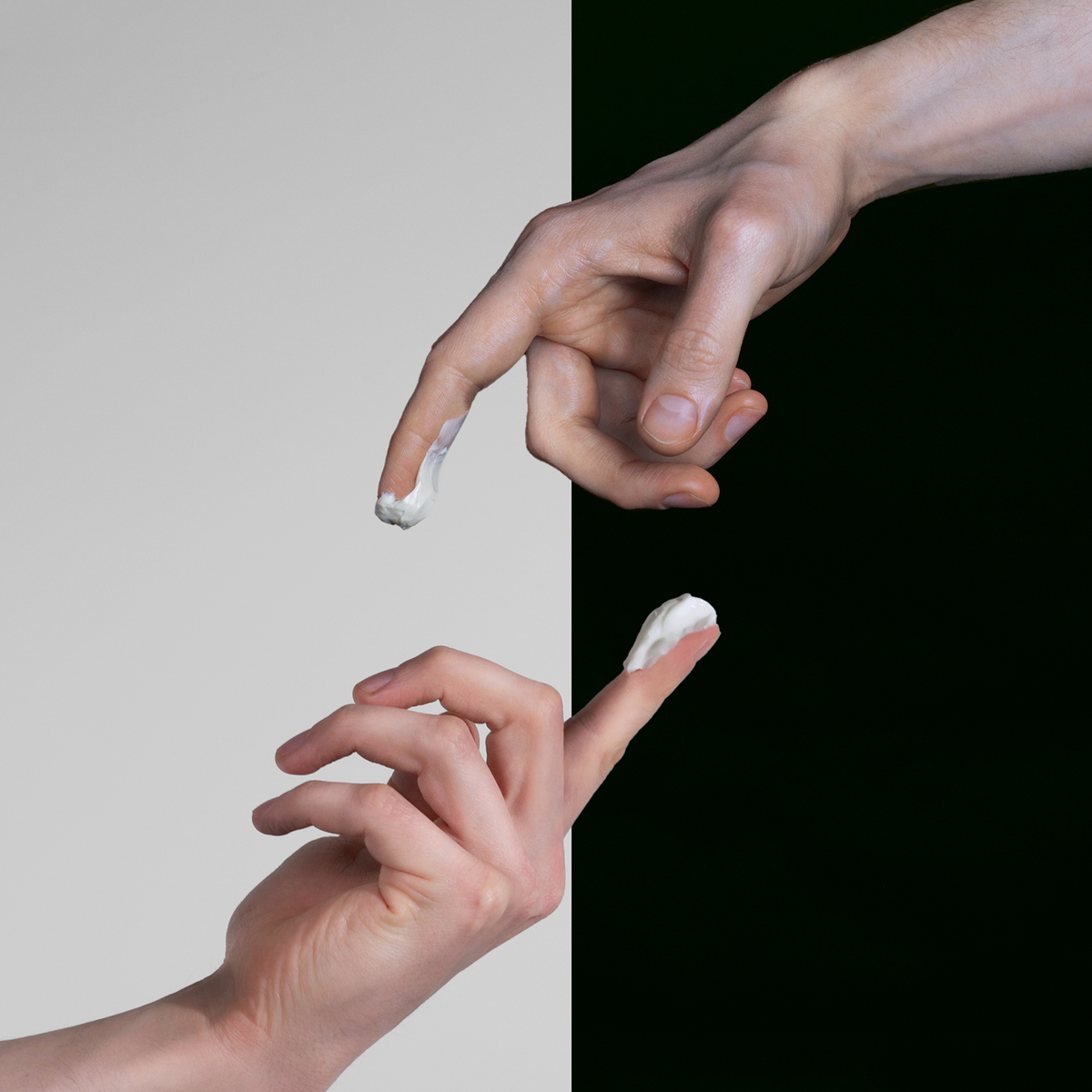 Zwei Hände mit Creme auf den Fingerspitzen vor kontrastreichem, zweigeteiltem Hintergrund.