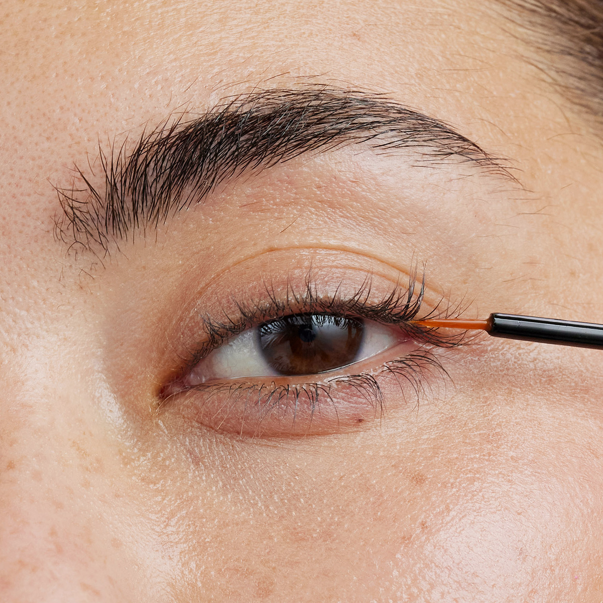 Eine Nahaufnahme einer Person, die das Xlash Eyelash Serum mit einem dünnen Pinsel auf den oberen Wimpernkranz aufträgt.