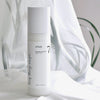 Eine Flasche Heartleaf 70 Daily Lotion steht auf einer weißen Fläche mit zartgrünen Blättern im Hintergrund.