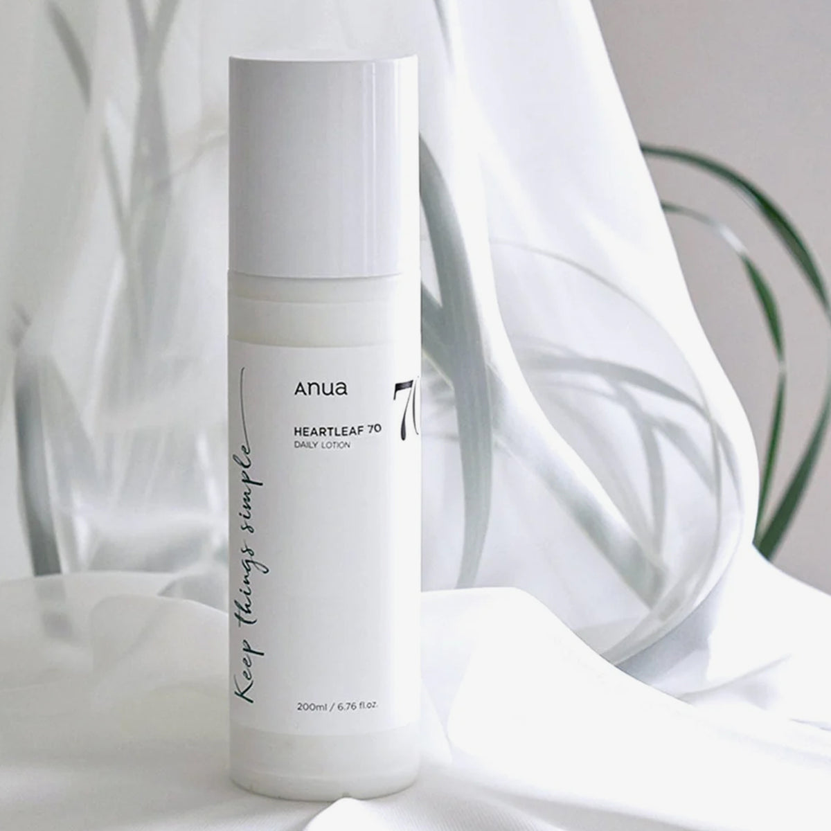 Eine Flasche Heartleaf 70 Daily Lotion steht auf einer weißen Fläche mit zartgrünen Blättern im Hintergrund.
