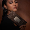 Eine Frau mit Smokey-Eye-Make-up hält die Groundwork-Palette – Defining Neutrals vor einem braunen Hintergrund.