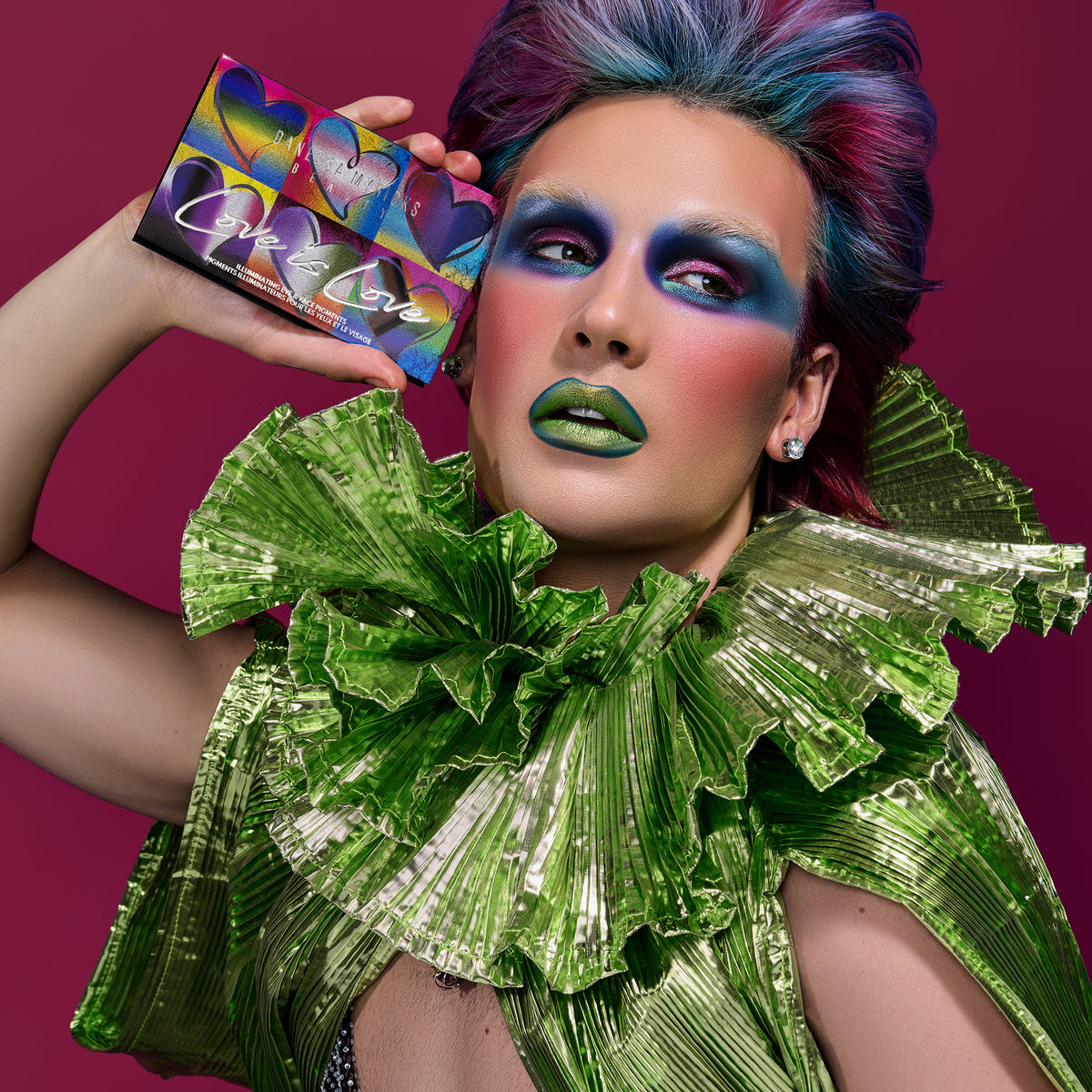 Person mit kräftigem, farbenfrohem Make-up und Haaren hält die Love is Love-Palette.