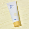Weiße Tube Seven Layer Ceramide Cream auf einem cremegelben strukturierten Hintergrund.
