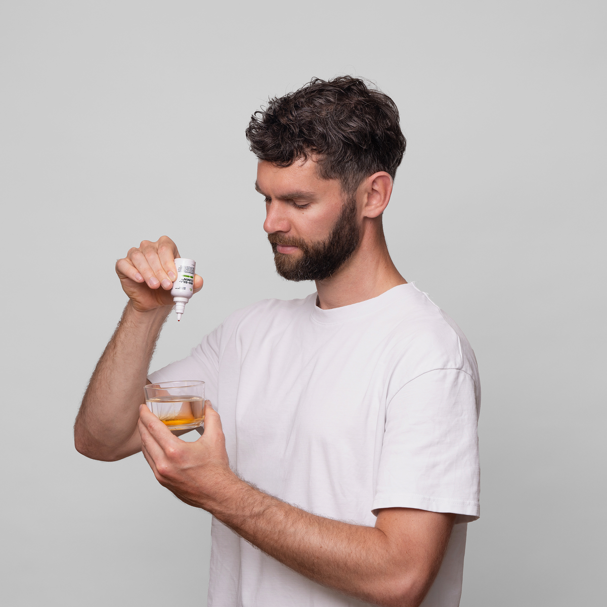 Ein Mann in einem weißen Shirt gibt orangenes Bio-Silacumin von Scandinavian Biolabs aus einer kleinen Flasche in ein Glas Wasser.