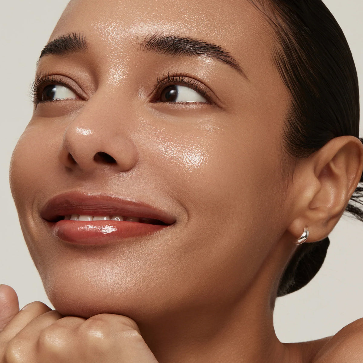 Mit strahlender, frischer Haut nach der Verwendung des Rice 70 Glow Milky Toner lächelt eine Frau sanft und stützt ihr Kinn auf ihre Hände.
