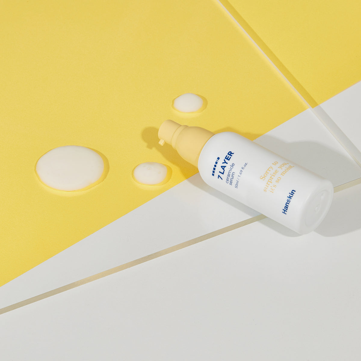 Eine Flasche Seven Layer Ceramide Serum und Lotionstropfen auf einem gelb-weißen Hintergrund.