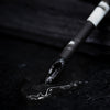 Ein Shadow Potion Paint Black Base Eclipse-Applikator wird in eine glänzende auf einer schwarzen Oberfläche dargestellt.