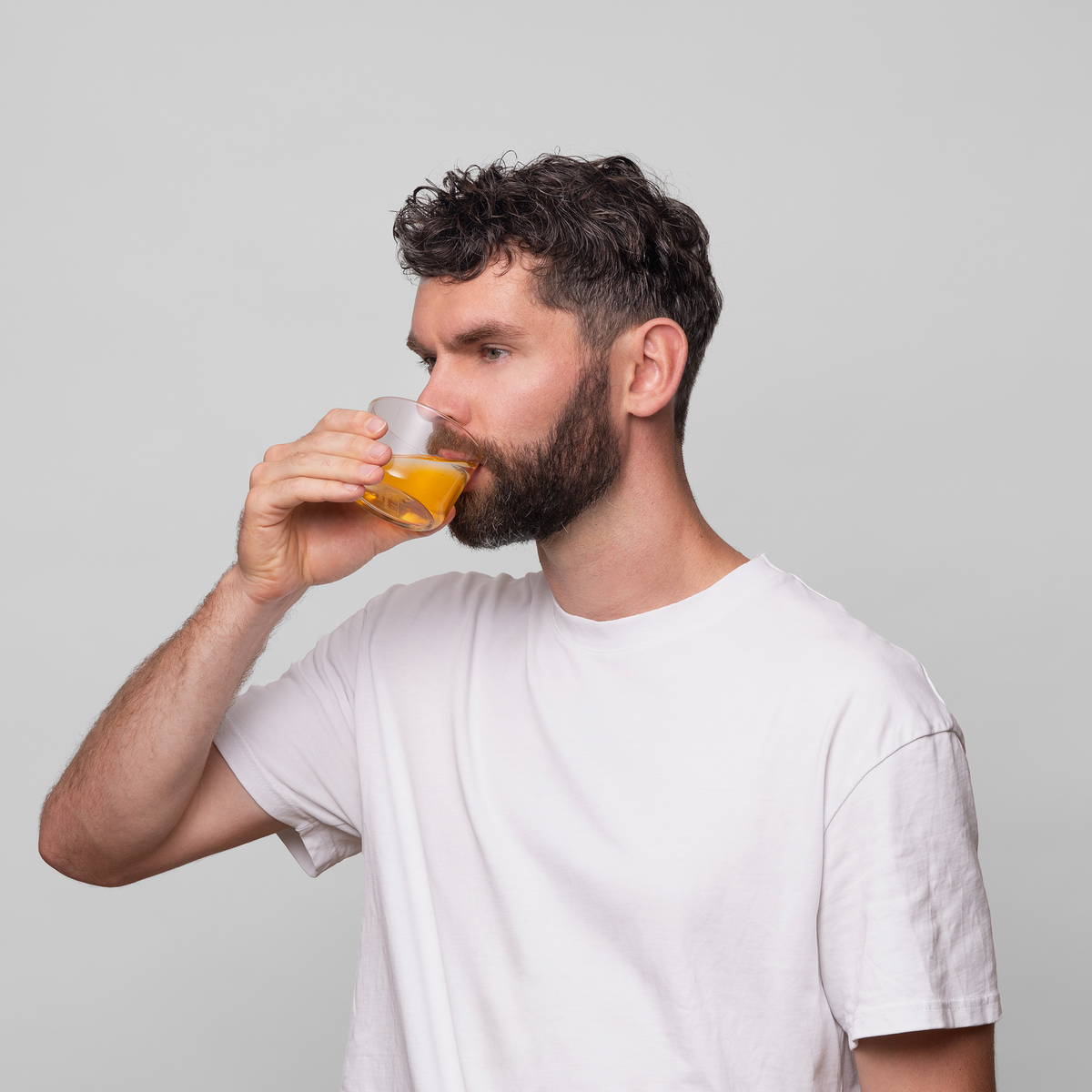 Ein Mann mit dunklen Haaren und einem Bart trägt ein weißes T-Shirt und trinkt Bio-Silacumin von Scandinavian Biolabs.