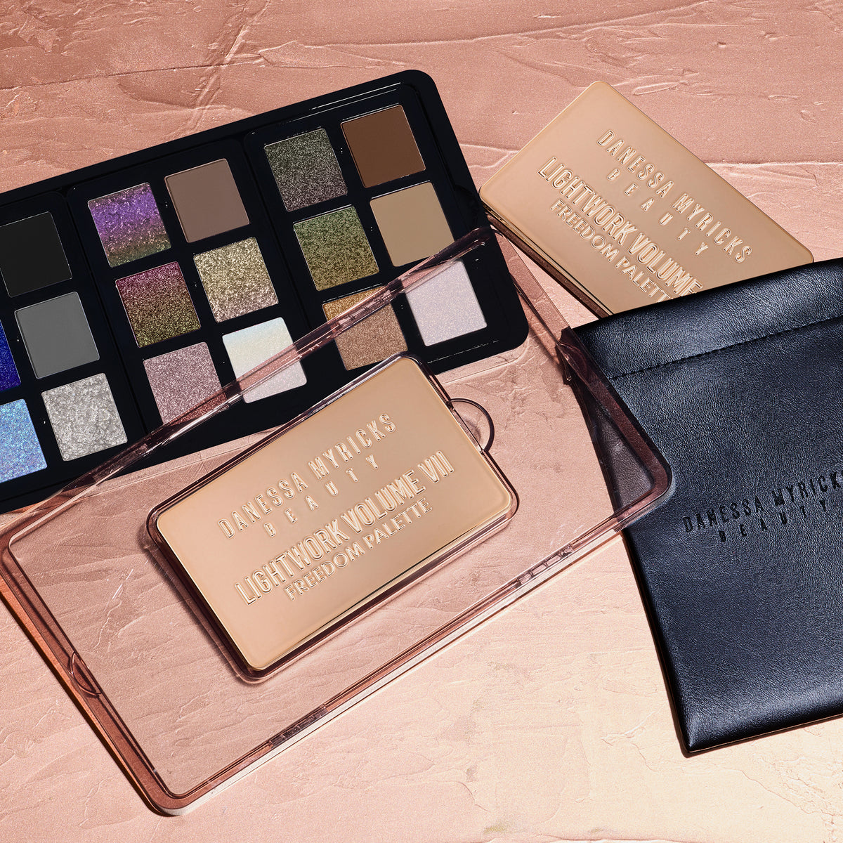 Die Danessa Myricks Beauty Lightwork Palette VII Freedom Palette wird neben einem schwazen Etui auf einer strukturierten, pfirsichfarbenen Oberfläche gezeigt.