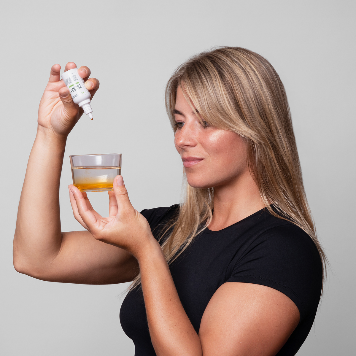 Eine Frau in einem schwarzen Shirt gibt Bio-Silacumin von Scandinavian Biolabs aus der Flasche in ein Glas und die Flüssigkeit färbt sich orange.