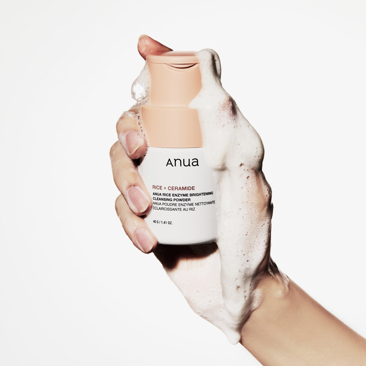 Eine Hand hält eine schaumige Flasche Rice Enzyme Brightening Cleansing Powder vor einem weißen Hintergrund.