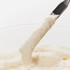 Ein Metallspatel hebt das Rice Enzyme Brightening Cleansing Powder aus seiner Schale.