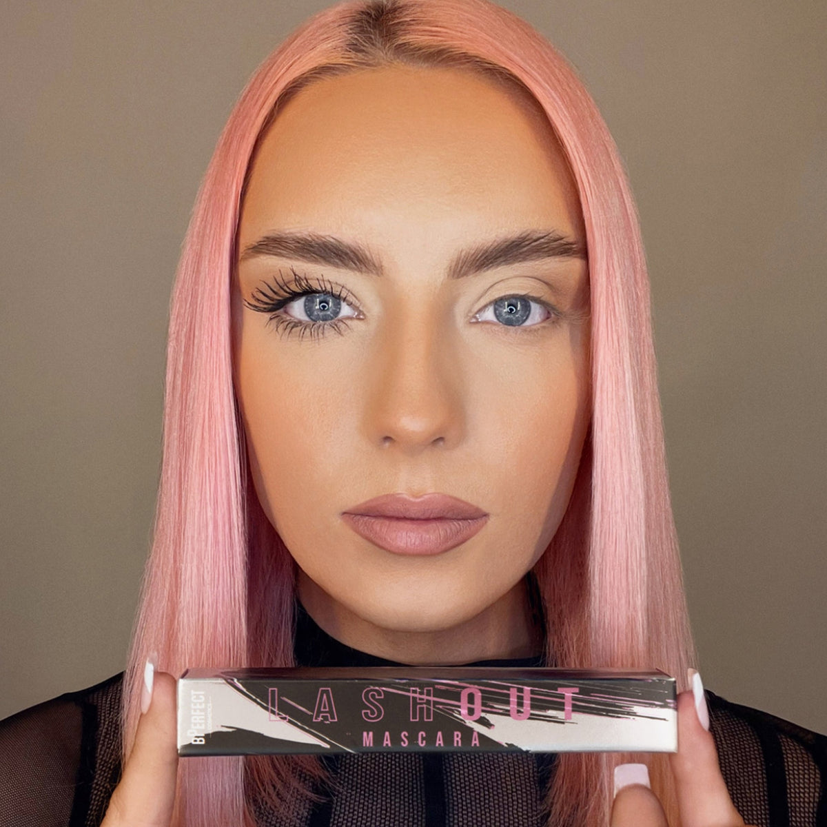 Eine Frau mit rosa Haaren demonstriert die Wirkung von Lash Out Mascara, indem sie ein Auge mit und eines ohne Mascara zeigt.