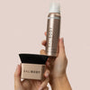 Zwei Hände halten den Bali Body Blending Brush und das Instant Tan Spray – Selbstbräuner-Set in roségoldener Verpackung vor neutralem Hintergrund.