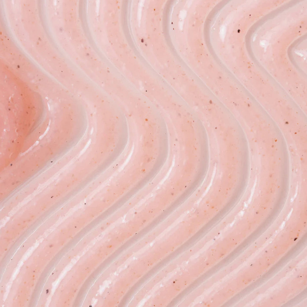 Nahaufnahme des rosa strukturierten Peelings mit wellenförmigen, erhabenen Linien und kleinen Partikeln.