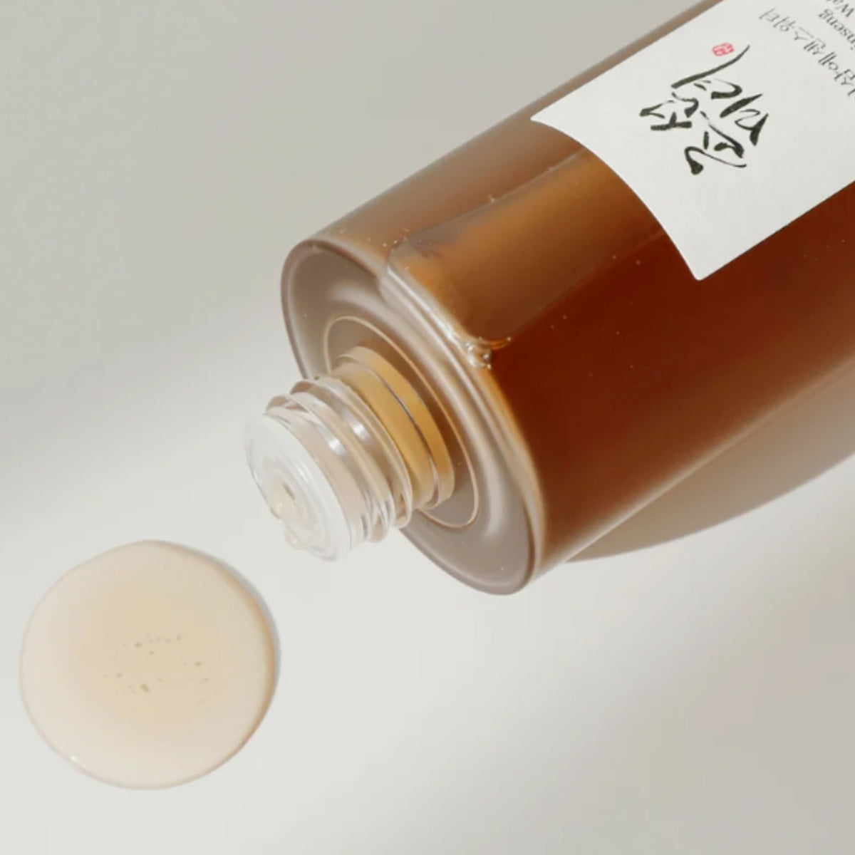 Nahaufname des Ginseng Essence Waters mit brauner Flüssigkeit und einem Tropfen auf beiger Oberfläche
