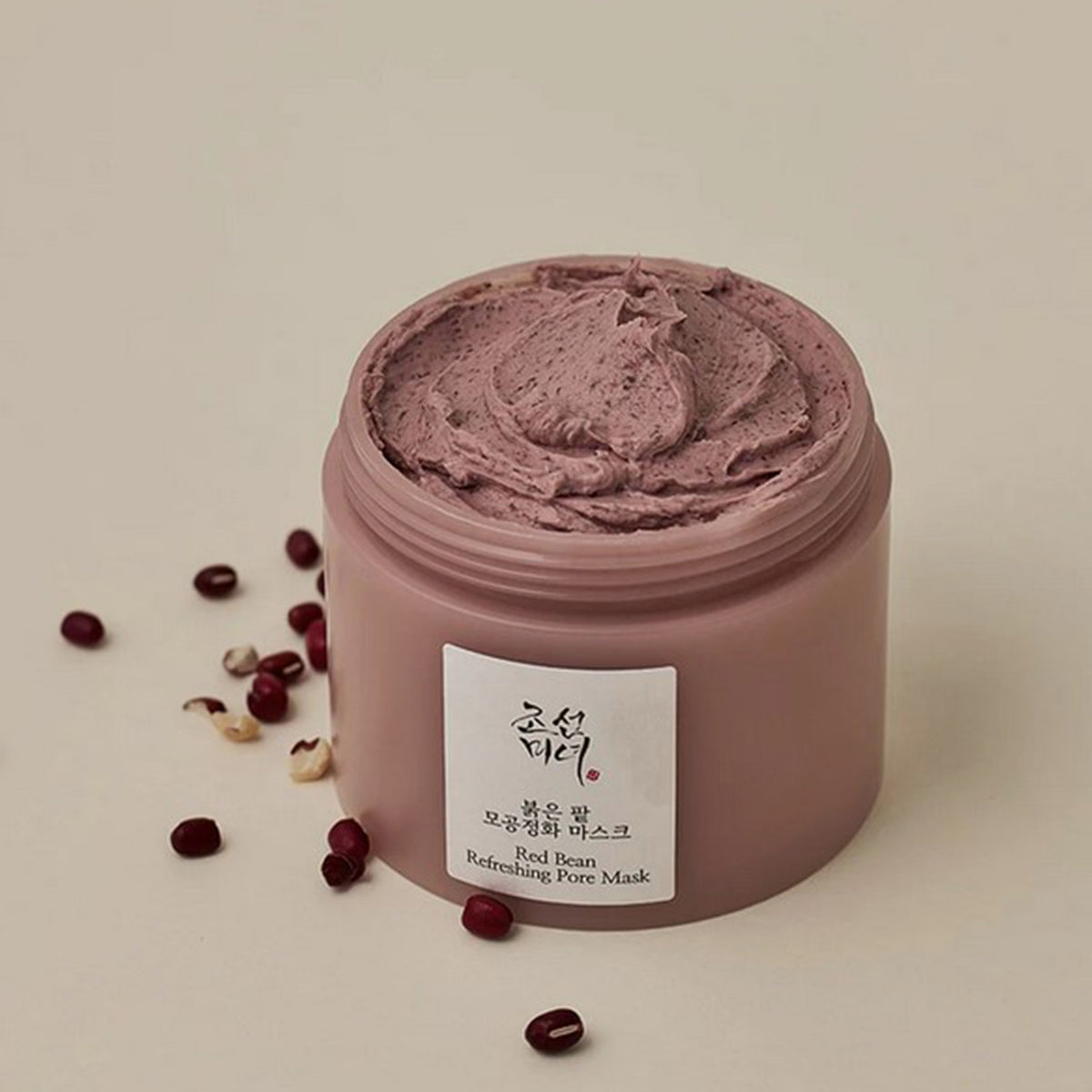 Ein offener Tiegel mit der braunen strukturierten Red Bean Refreshing Pore Mask auf salbeigrüner Oberfläche