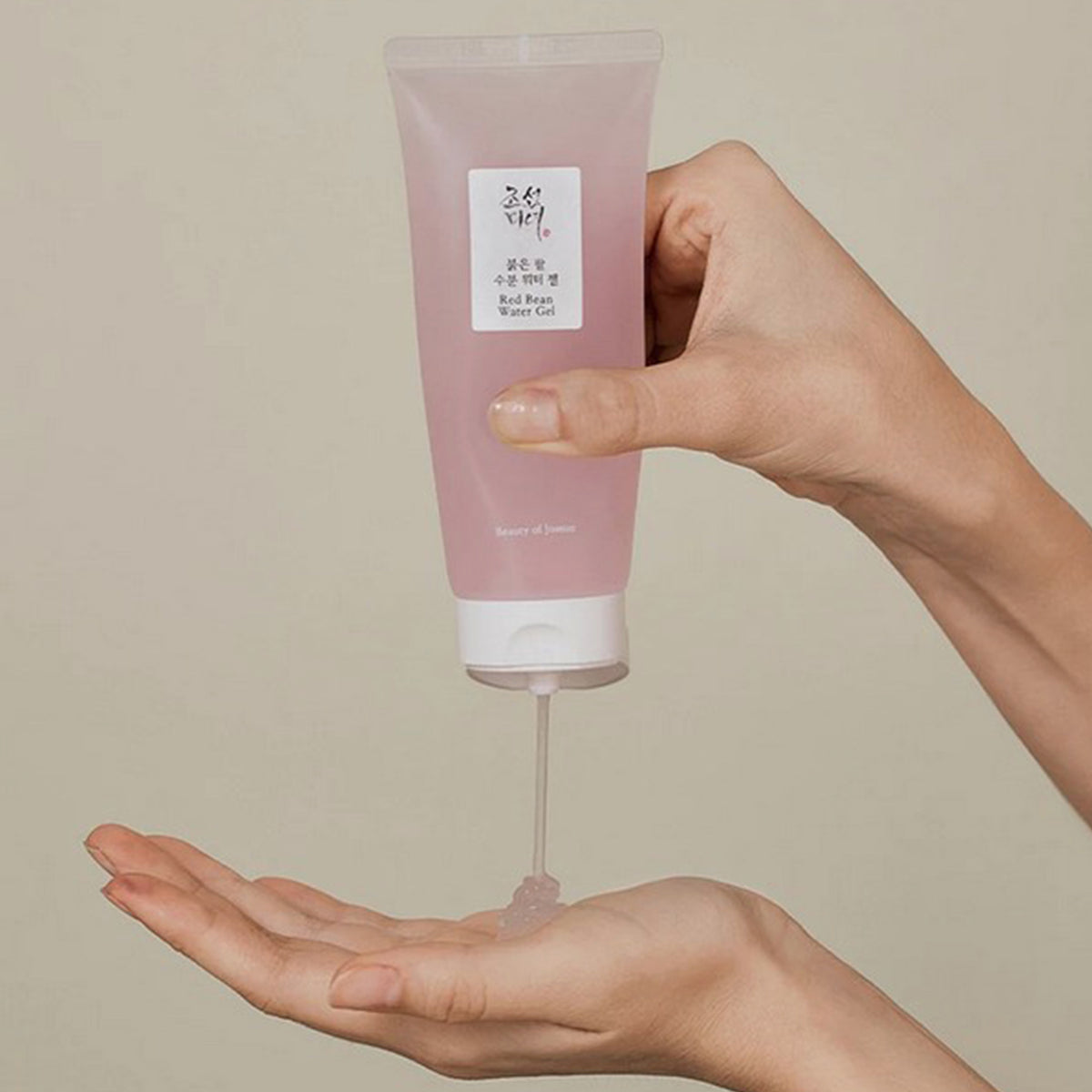 Jemand gibt Red Bean Water Gel vor salbeigrünem Hintergrund aus einer rosa Tube in die Hand