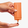 Eine Hand drückt die Technocolor Self Tanning Face Serum aus einer orangefarbenen Flasche auf ihr Fingerspitzen.