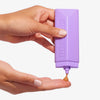 Eine Person drückt vor einem weißen Hintergrund Technocolor Self Tanning Face Serum Magenta auf ihre Fingerspitzen.