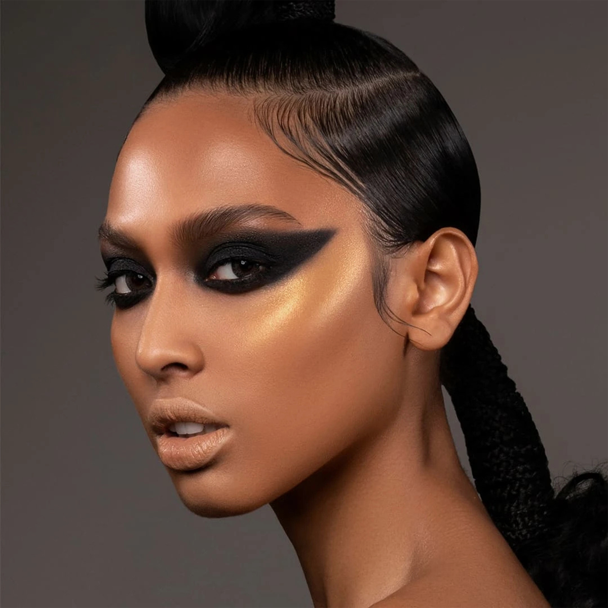 Frau mit glattem Haar, kräftigem schwarzem Winged Eyeshadow und goldenem Wangenknochen-Highlight mit Danessa Myricks Beauty Balm Contour.