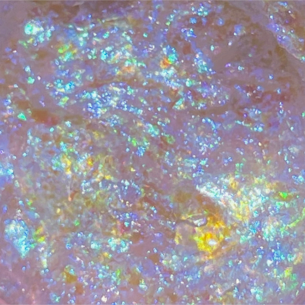 Nahaufnahme von Danessa Myricks Beauty Infinite Chrome Flakes Strobe Light, die eine irisierende Oberfläche mit schimmernden blauen, gelben und grünen Glitzern zeigen.